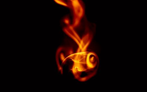 Captivating image of a swirling orange flame against a dark background. Ideal for themes of heat and energy.